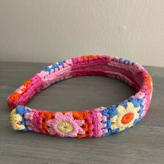 a crocheted headband with colorful flowers on the top and bottom, sitting on a table