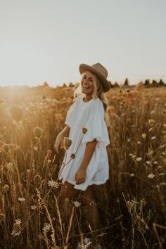 a woman is standing in the middle of a field with tall grass and wildflowers