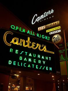 a restaurant sign lit up at night with other signs in the back ground and on top of it