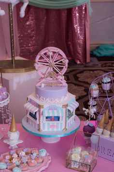 a table topped with lots of cakes and desserts next to a ferris wheel on top of a pink table cloth