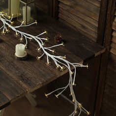 a wooden table topped with a white candle and some branches covered in lights next to a mirror