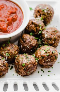 meatballs with sauce and parsley on a white plate next to a small bowl