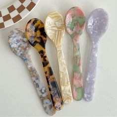 four different colored plastic spoons sitting next to each other on a white counter top