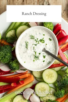 a bowl of ranch dressing surrounded by vegetables and cucumbers on a white plate