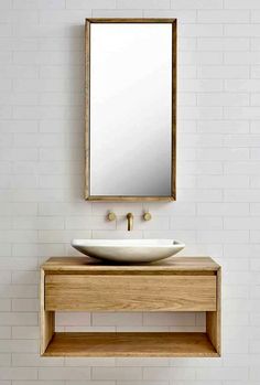 a bathroom sink sitting under a mirror on top of a wooden shelf next to a white tiled wall