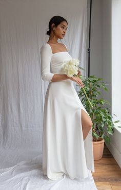 a woman in a white dress is holding a flower and posing for the camera with her leg up