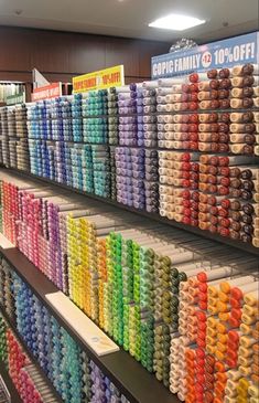 rows of different colored spools of thread on display in a store with lights