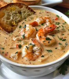 a bowl of soup with shrimp and bread on the side