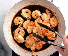 a person stirring shrimp in a pot with tongs