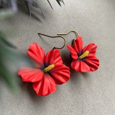 two red flower shaped earrings sitting on top of a cement floor next to a plant