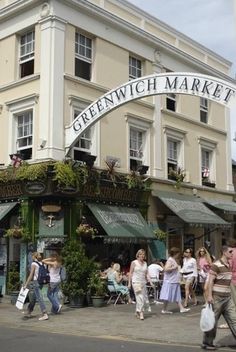 people walking on the street in front of a market with an arch over it that says greenwich market