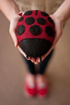 a ladybug stuffed animal being held by a child's hands with red slippers