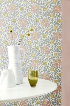 two vases on a table with flowers in front of a wallpapered background