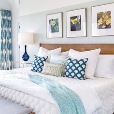 a bedroom with blue curtains and white bedding, two pictures on the wall above the bed