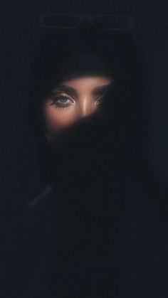 a woman with dark clothing and glasses on her face is seen through the hood in the dark