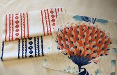 three pieces of cloth with designs on them sitting on a tablecloth covered in white and blue fabric