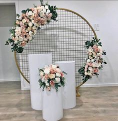 three white vases with pink and white flowers in front of a circular wall decoration