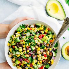 a person holding a white bowl filled with black eyed peas, corn and avocado