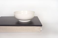 a white bowl is sitting on top of a book and it's resting on the edge