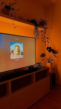 a flat screen tv sitting on top of a wooden entertainment center next to a potted plant