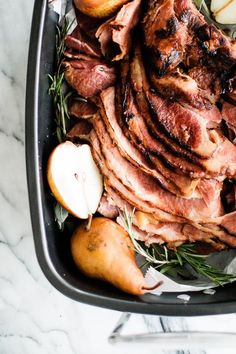 a roasting pan filled with meat, potatoes and apples on top of a marble counter