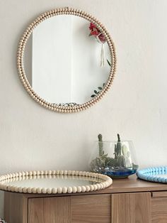 a round mirror sitting on top of a wooden dresser next to a vase filled with flowers