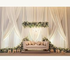 a couch sitting in front of a white curtained wall with candles and flowers on it