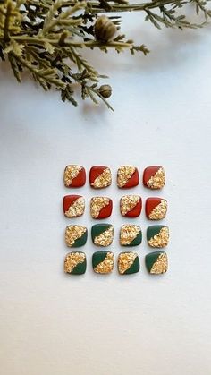 gold and red glittered nail tips on a white surface next to evergreen branches with pine cones in the background