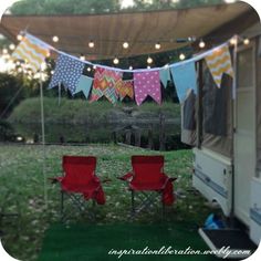 two red chairs sitting in front of a camper with bunting on the grass