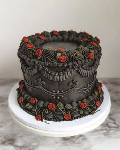 a three tiered cake with red roses on the top and black icing, sitting on a white plate