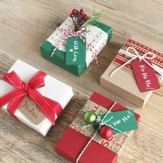 three wrapped christmas gifts sitting on top of a wooden table with red and green ribbons