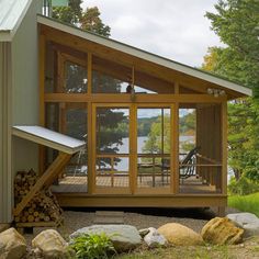 a small cabin with a porch and deck on the side of it, surrounded by rocks