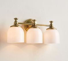 three light bathroom fixture with frosted glass shades on white wall and gold metal frame