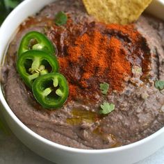 a white bowl filled with black bean dip next to a tortilla chip and cilantro