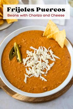 a white bowl filled with beans and cheese next to tortilla chips