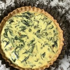 a quiche with spinach and cheese in a pie pan on a marble counter