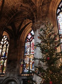 a decorated christmas tree in the middle of a church with stained glass windows behind it