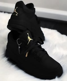 a pair of black sneakers with gold accents on them sitting on a white fur surface