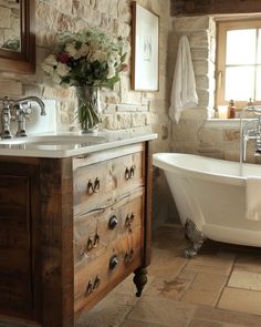 a white bath tub sitting under a window next to a wooden sink vanity with drawers