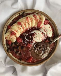 a bowl filled with bananas, strawberries and other toppings next to a spoon