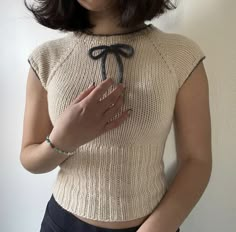 a woman with short hair wearing a sweater and holding her hand up to her chest