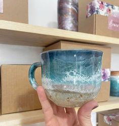 a hand holding a blue and white coffee cup in front of shelves with other items