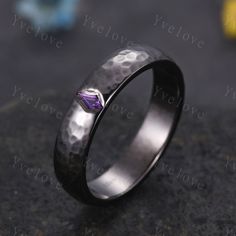 a wedding band with a purple diamond in the center on top of a black surface