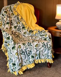 a chair with a yellow blanket on top of it next to a table and lamp