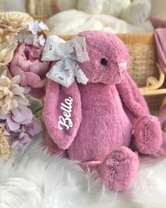 a pink teddy bear sitting on top of a white fur covered floor next to flowers