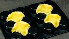 four cupcakes with yellow frosting in a black muffin tin