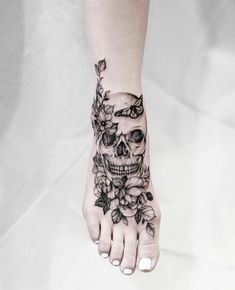 a woman's foot with a skull and flowers tattoo on it