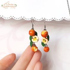 a pair of oranges with leaves and flowers hanging from earrings