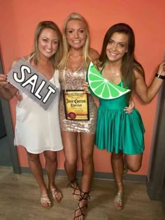 three young women posing for a photo in front of a pink wall holding up signs