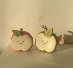 two ceramic apples with faces painted on them, one has a worm in it's mouth